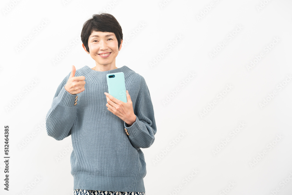 スマートフォンを持ちながらサムズアップをするミドル女性