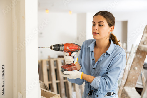 Fototapeta Woman drilling hole in wall with screwdriver in a repairable room
