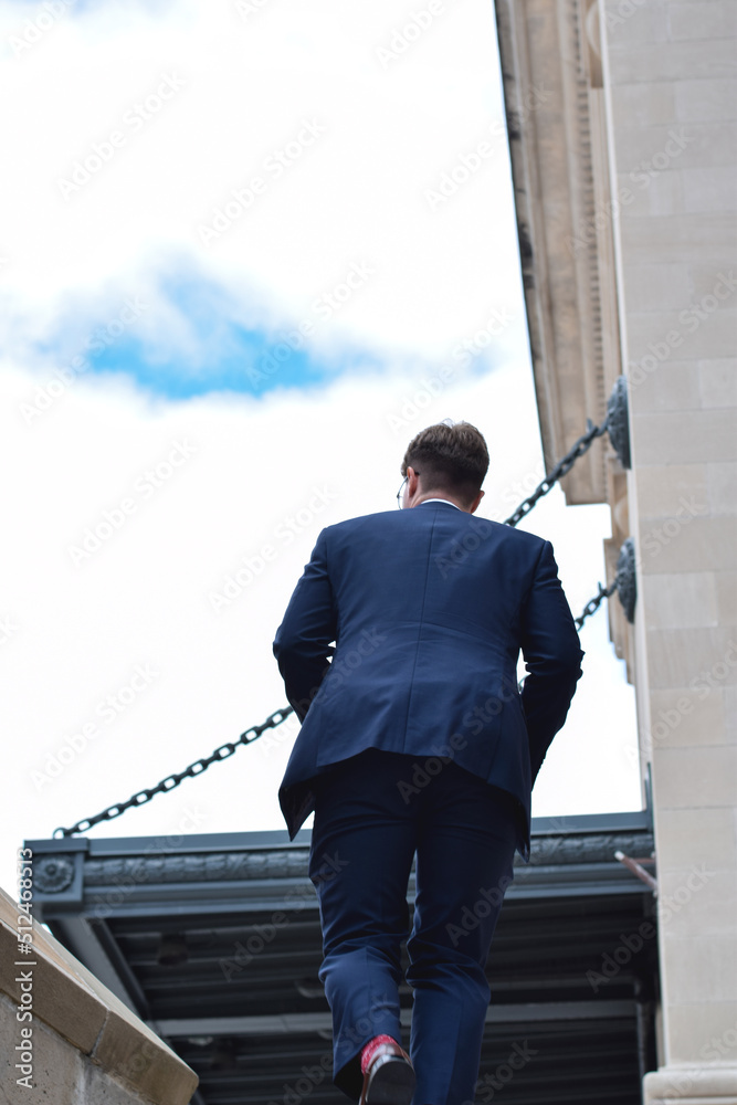 Young businessman in suit from behind coming up stairs on city street Young businessman in suit from behind coming up stairs on city street