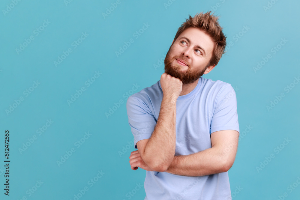 Portrait of smiling happy bearded man looking away with pensive expression, dreaming pleasant thoughts, fantasizing and making wish. Indoor studio shot isolated on blue background. Portrait of smiling happy bearded man looking away with pensive expression, dreaming pleasant thoughts, fantasizing and making wish. Indoor studio shot isolated on blue background.