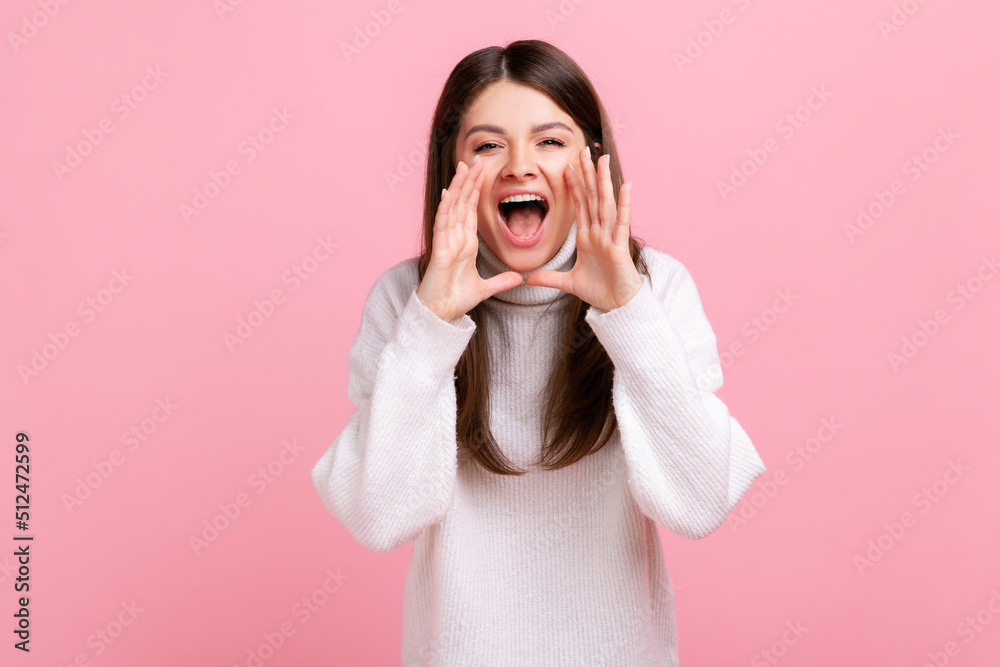 Portrait of young adult brunette female standing, holding arms near wide open mouth and screaming, wearing white casual style sweater. Indoor studio shot isolated on pink background. Portrait of young adult brunette female standing, holding arms near wide open mouth and screaming, wearing white casual style sweater. Indoor studio shot isolated on pink background.