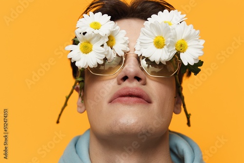 a close portrait of a handsome  funny man with daisies on his eyes  standing on a bright background in a light blue hoodie