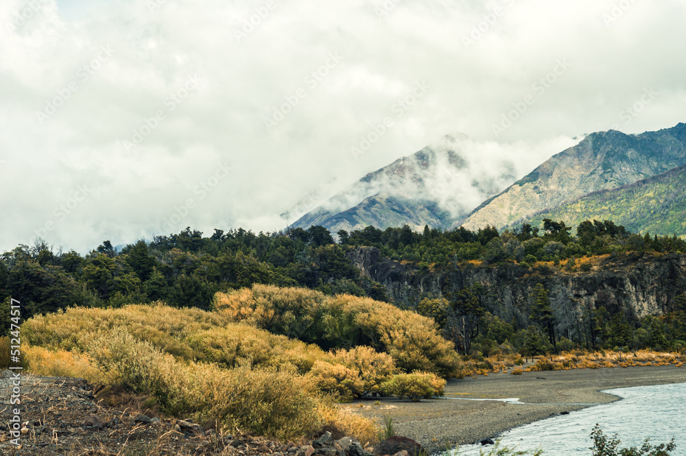 Forest with snowy mountains and mist on the shore of a lake in autumn. Los Alerces National Park