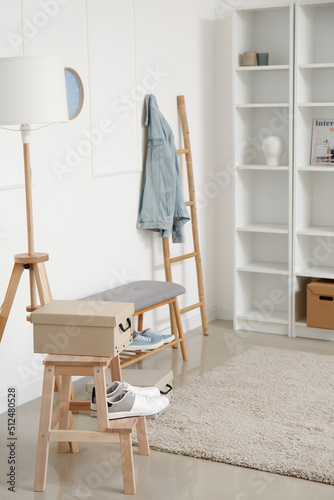 Stylish shelf unit and soft bench with shoes near white wall © Pixel-Shot