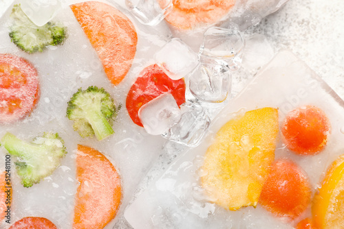 Fresh cut vegetables frozen in ice on light background