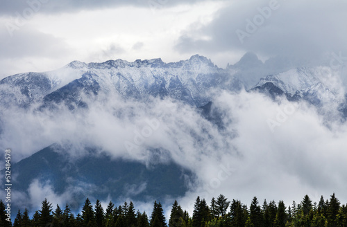 Beautiful mountain snowy peaks of the Eastern Sayan Mountains are covered with low clouds on a cloudy day. Natural mountain background