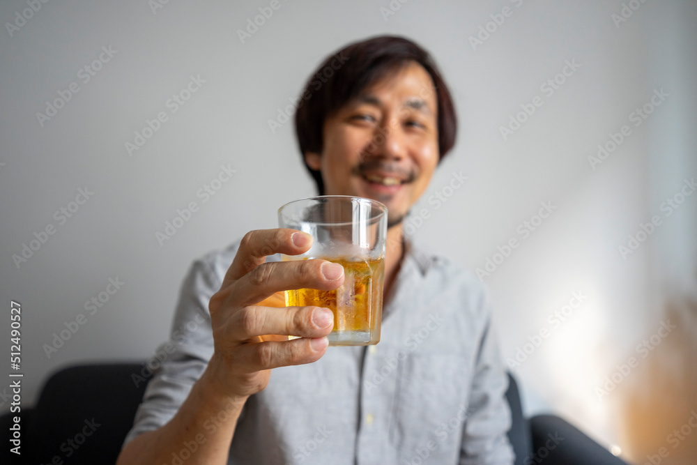 Asian man sitting on sofa enjoy a glass of whiskey. Focus on the glass. Alcohol drinking concept. Asian man sitting on sofa enjoy a glass of whiskey. Focus on the glass. Alcohol drinking concept.