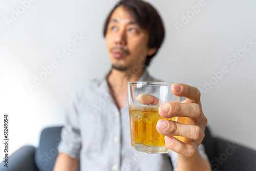 Asian man sitting on sofa enjoy a glass of whiskey. Focus on the glass. Alcohol drinking concept.