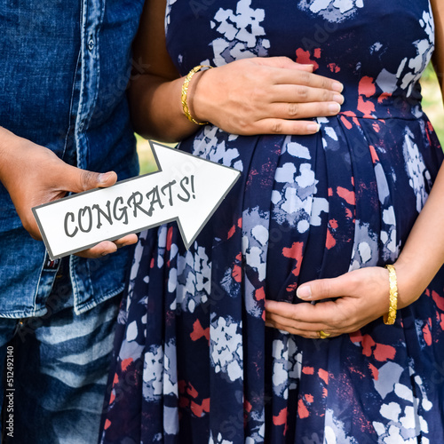 Indian couple posing for maternity baby shoot. The couple is posing in a lawn with green grass and the woman is falunting her baby bump in Lodhi Garden in New Delhi, India