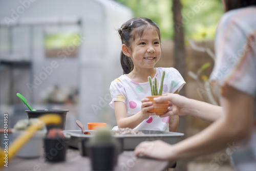 The smiling little girl helps her mother working in cactus garden.
