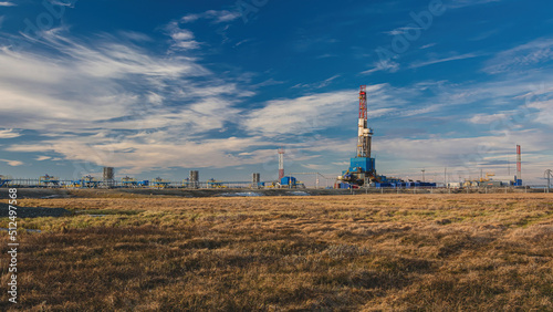 Oil and gas field in the Arctic. Spring. Drilling rig for drilling wells. The landscape of the northern tundra is in front. On the left is the infrastructure of wells for gas production. Beautiful sky