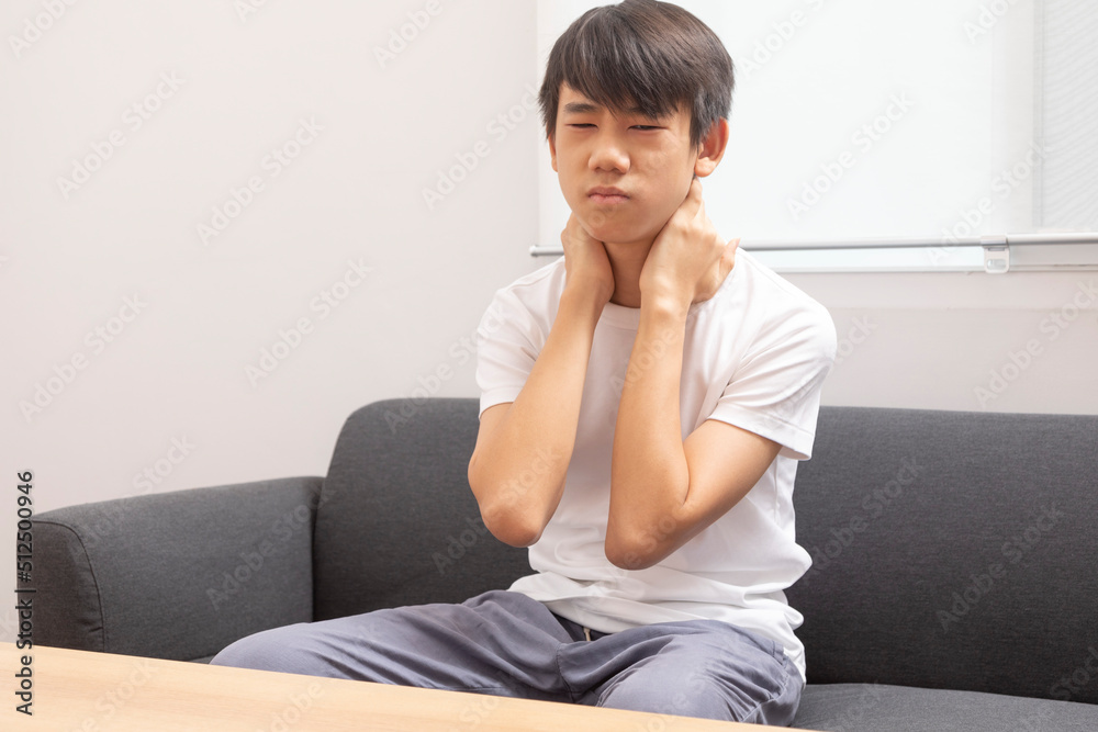 Early osteochondrosis. Teenage boy holding his hand behind his neck sitting on sofa at home. Early osteochondrosis. Teenage boy holding his hand behind his neck sitting on sofa at home.