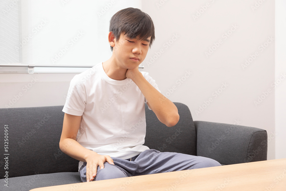 Early osteochondrosis. Teenage boy holding his hand behind his neck sitting on sofa at home. Early osteochondrosis. Teenage boy holding his hand behind his neck sitting on sofa at home.