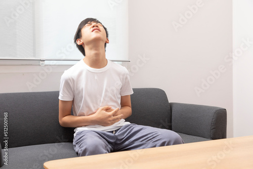 Asian Teen boy suffering from stomachache sitting on sofa at home.