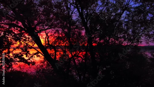Spectacular red dawn sky mirrored in tranquil waters, dynamic moving perspective.
