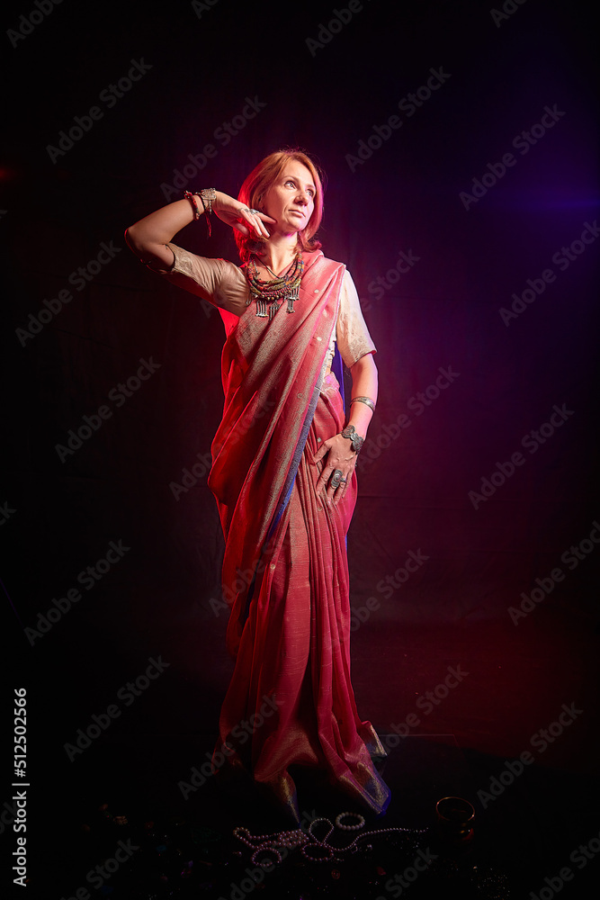 A beautiful European woman in a traditional Indian sari on a black background. Girl model posing in the studio