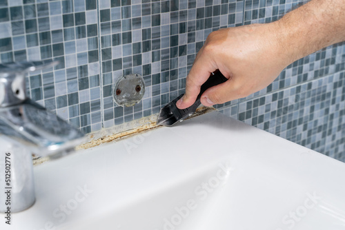 dirty grouts in the bathroom and moldy tiles. master cleans dirt with a tool. hands close up