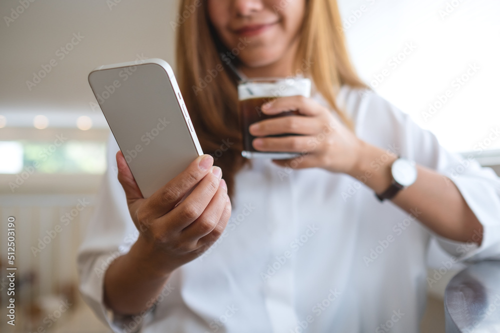 Closeup of a young woman holding and using mobile phone while drinking coffee in cafe Closeup of a young woman holding and using mobile phone while drinking coffee in cafe