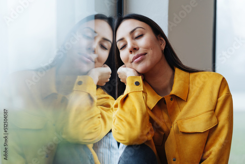 Young woman leans relaxed on the window and has her eyes closed