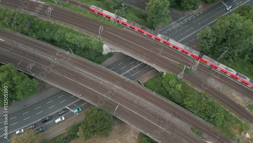 Birds eye view of a railway bridge crossing a big street with a red commuter train crossing the bridge to the north. Cologne, Germany June 2022 photo