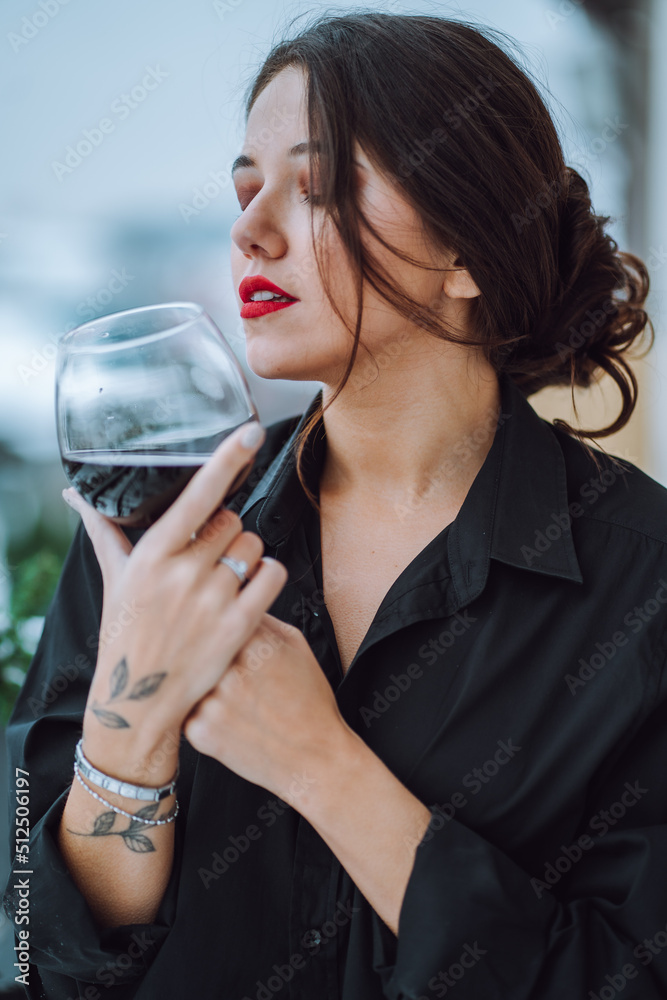 Portrait of young gorgeous woman with beautifully coiffured dark hair, make-up wearing black shirt, holding glass with red wine, closing eyes, enjoying taste. Celebration, birthday, holiday. Vertical. Portrait of young gorgeous woman with beautifully coiffured dark hair, make-up wearing black shirt, holding glass with red wine, closing eyes, enjoying taste. Celebration, birthday, holiday. Vertical.
