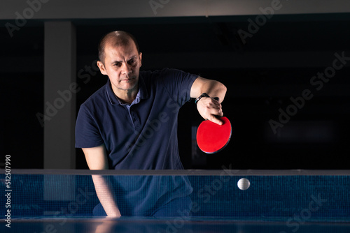 A man plays table tennis. Photographed in low key, there is artistic noise.