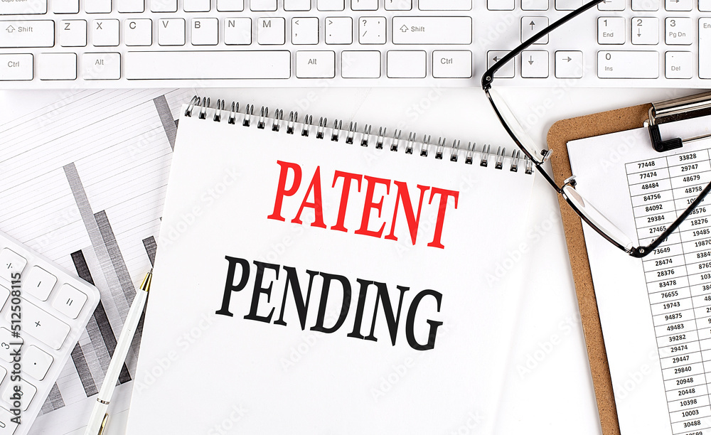 Text PATENT PENDING on Office desk table with keyboard, notepad and analysis chart on white background. Text PATENT PENDING on Office desk table with keyboard, notepad and analysis chart on white background.