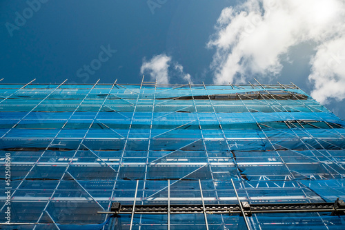 Building in scaffolding and blue mesh net matching blue cloudy sky. Construction and renovation industry in town. photo