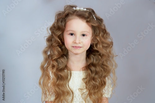 Portrait of beautiful cute pretty kid child girl with curly hair looking at camera in dress On grey background 