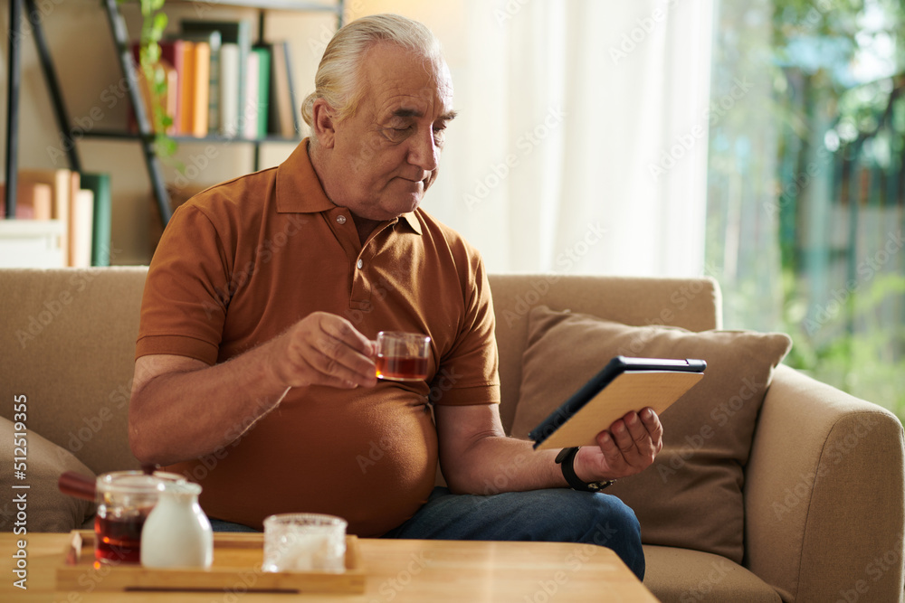 Senior man drinking tea and watching news on tablet computer in the morning Senior man drinking tea and watching news on tablet computer in the morning