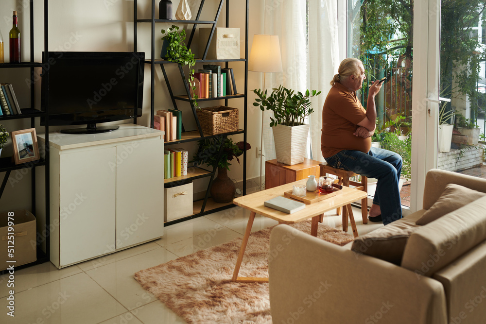 Pensive senior man looking outside when recording voice message for friend or family member Pensive senior man looking outside when recording voice message for friend or family member