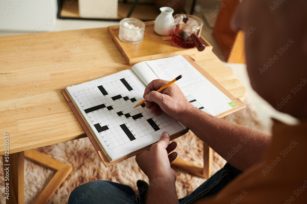 Hands of senior man solving crossword puzzle when spending day at home