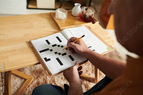 Canvas Print Hands of senior man solving crossword puzzle when spending day at home