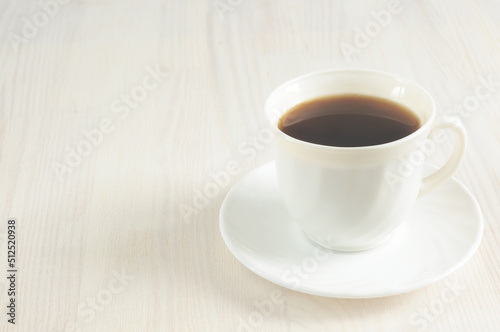 A cup of invigorating black coffee on a light wooden background. Selective focus, toned image, natural light. copy space for text