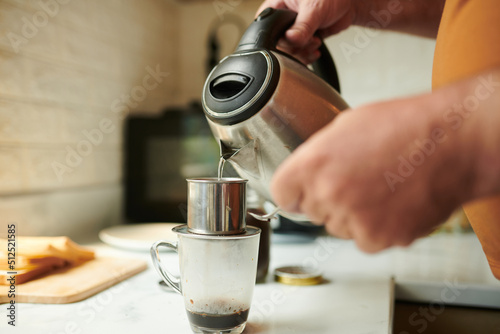 Closeup image of man pouring hot water in phin filter when making cup of coffee at home © DragonImages