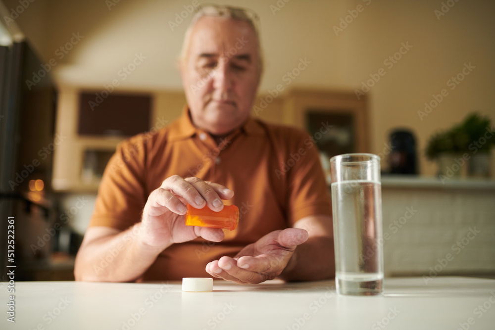Serious aged man taking pills with glass of water after breakfast