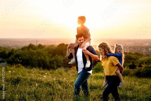 Family with two daughters walking at the meadow during the sunset