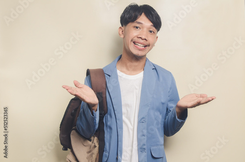 young man wearing college suit gesturing up while carrying laptop and backpack on isolated background