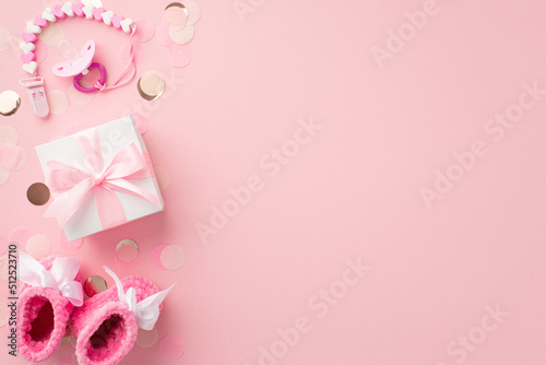 Baby accessories concept. Top view photo of white giftbox with bow pacifier chain pink knitted booties and shiny confetti on isolated pastel pink background with copyspace © ActionGP