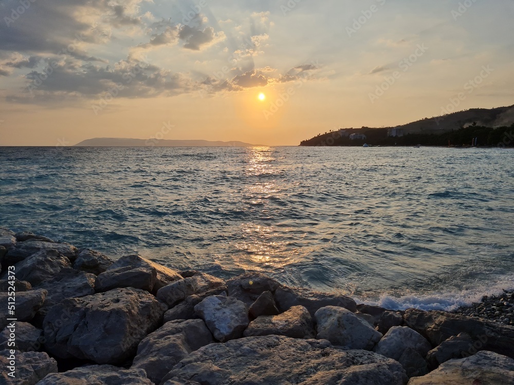 Scenery with sunset on the beach. Sunset over the sea. Scenic landscape with surf on waves in the evening. Beautiful sun rays at sunset. Time lapse twilight. Panoramic view of pebble beach and stones.