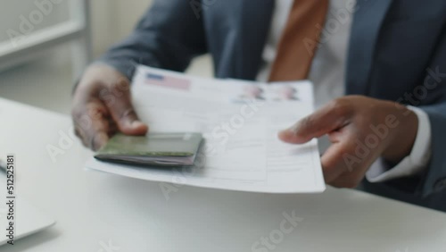 Close up tilt up shot of African American visa officer taking documents and passport form applicant and asking questions during interview in U.S. embassy photo