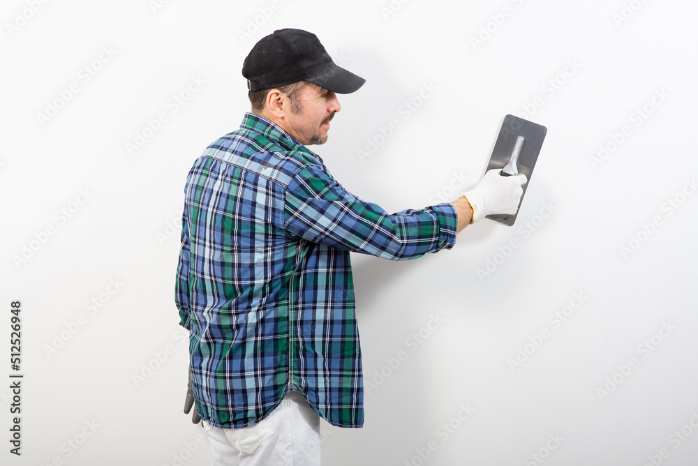 Male builder in a cap plastering a white wall
