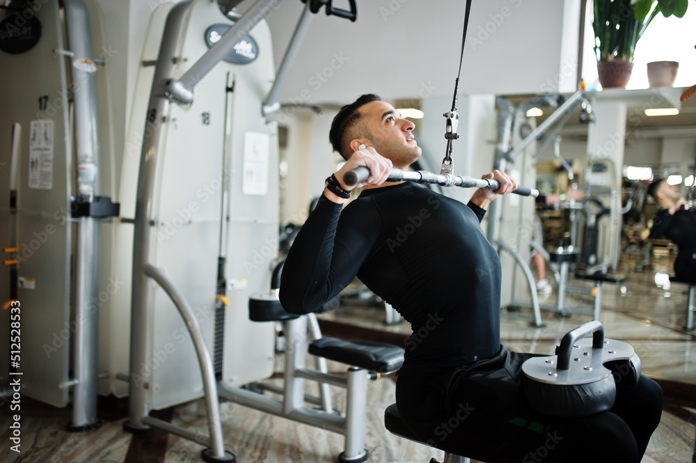 Muscular arab man training and doing workout on fitness machine in modern gym. Muscular arab man training and doing workout on fitness machine in modern gym.