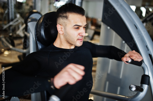 Muscular arab man training and doing workout on fitness machine in modern gym.