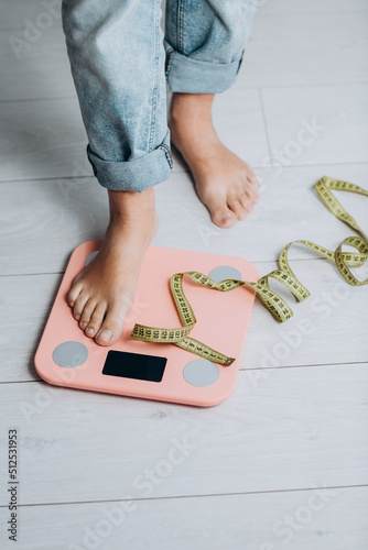 Female standing on the weight scale in the white bathroom floor with green curtain in background