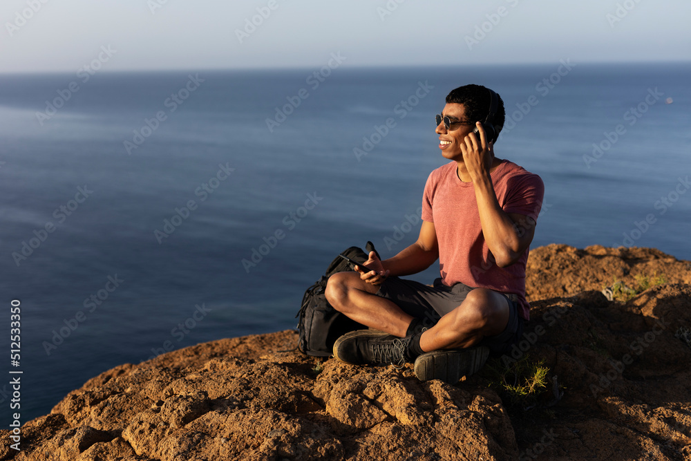 Young man sitting on the stone listening the music. Tourist man on the top of the mountain