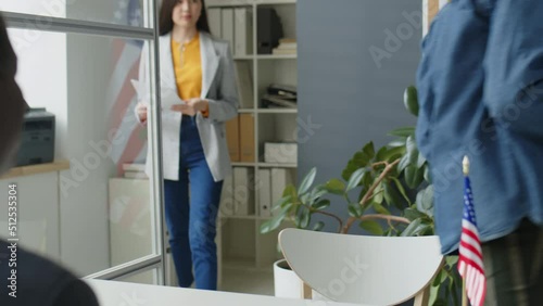 Young Asian woman walking in U.S. embassy after Caucasian man, giving application form to African American officer and speaking with him during visa interview photo