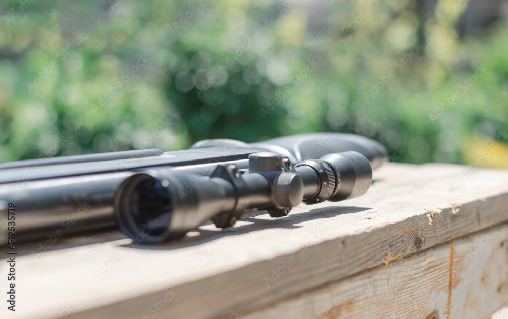 Obraz premium Sniper rifle lies on a wooden background. Optical sight close-up.