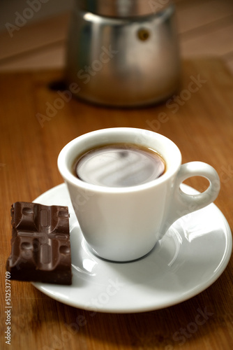 White cup of espresso coffee with piece of chocolate on plate