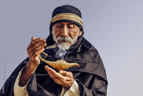 An old Arabic sorcerer holds an Aladdin's lamp and conjures.